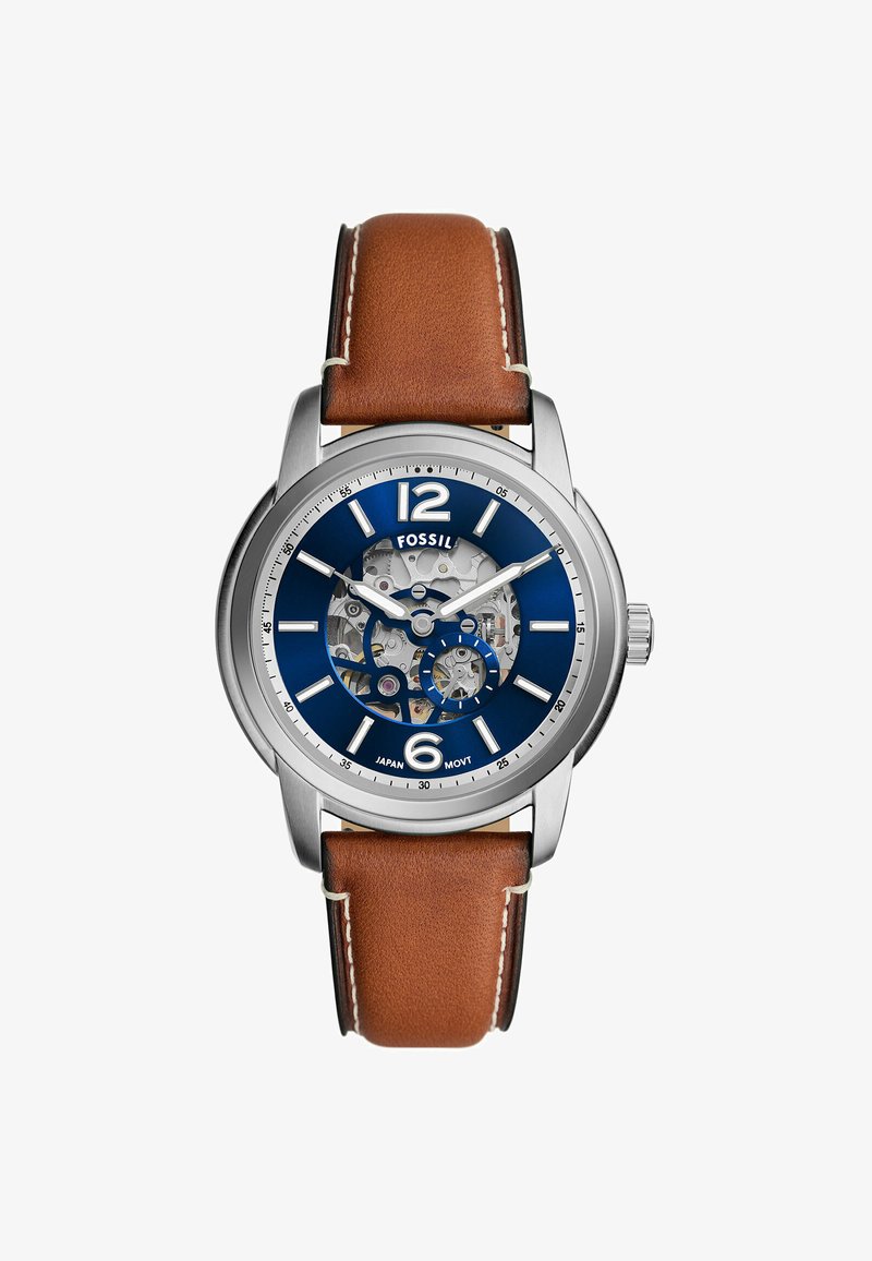 Fossil-Uhr mit einem Gehäuse aus silbernem Edelstahl, blauen Zifferblatt, transparentem Werk und braunem Lederarmband mit weißen Nähten.