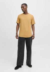 Sennepsgule T-shirt med korte ærmer og rund hals, parret med løstsiddende sorte denimbukser og sorte sko. Minimalistisk design, blød tekstur.