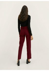 Pantalon sur mesure bordeaux taille haute et jambes droites. Haut noir à manches longues, avec des boutons décoratifs sur les manches. Texture lisse.