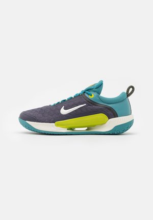 Nike juoksukengät, joissa on tummanlila verkko päällinen, teal-väriä yksityiskohtina, valkoinen Swoosh-logo, kirkkaankeltaisia yksityiskohtia ja ainutlaatuinen vihreä välipohja.