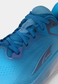 Chaussure de course bleue avec un dessus en mesh texturé, design à lacets, languette rembourrée et un logo bien visible sur le côté. Semelle légère.