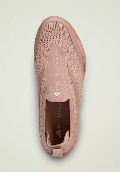 Zapato tipo slip-on en material de tejido rosa suave, con una superficie texturizada y acentos laterales distintivos. Marca visible a lo largo del costado.