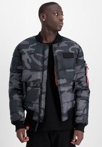 Giacca bomber imbottita in un motivo camouflage nero e grigio, con zip frontale, polsini a coste e un'accentuazione arancione sulla zip.