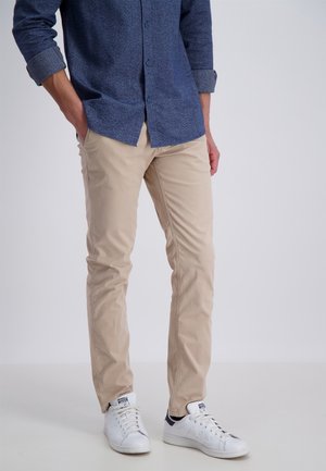 Chinos de algodón beige con corte slim, combinados con una camisa abotonada azul marino y zapatillas blancas, presentando una textura suave y detalles mínimos.