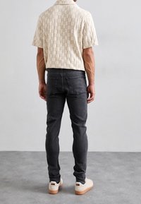 Lyhythihainen, kuvioitu beige paita, jossa ruutukuosi, yhdistetty kapealahkeisiin tummanharmaisiin farkkuihin ja valkoisiin tennareihin, joissa on kumipohjat.