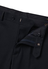 Marineblauwe, op maat gemaakte broek met een gestructureerd patroon, voorzien van een ritssluiting, knoopsluiting en twee steekzakken aan de voorkant. Detail van de tailleband zichtbaar.