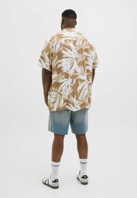 Chemise à manches courtes, marron avec des motifs de feuilles blanches ; assortie à un short en jean. Design simple, coupe décontractée, texture de tissu douce.
