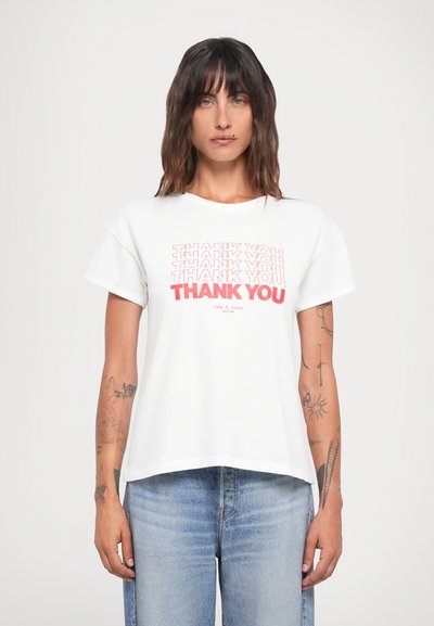 T-shirt bianco in cotone con la scritta audace "GRAZIE" in rosso, maniche corte e vestibilità comoda. Abbinato a jeans in denim blu chiaro.