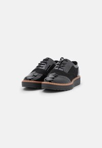 Scarpe in pelle nera con finitura lucida, accenti in camoscio, perforazioni decorative e una suola in gomma durevole con un leggero tacco.
