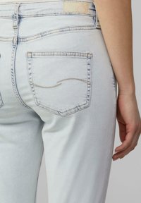 Jean en denim bleu clair avec un gros plan sur le dos, présentant deux poches plaquées avec des détails de couture subtils et une texture lisse.