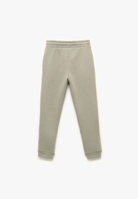 Helle graue Baumwoll-Jogginghosen mit einem elastischen Bund, schmal zulaufenden Beinen und seitlichen Taschen. Glatte Textur mit gerippten Bündchen an den Knöcheln.