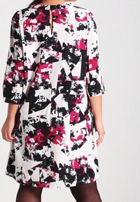 Mehrfarbiges Kleid mit einem auffälligen abstrakten Muster in Schwarz, Weiß und verschiedenen Rosatönen. Verfügt über drei Viertel lange Ärmel und ein Schlüssel-Ausschnitt-Detail auf der Rückseite.