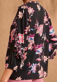 Blusa nera a fiori con motivi di fiori rosa, blu e bianchi, caratterizzata da un colletto arricciato e maniche a sbuffo, realizzata in un tessuto leggero.