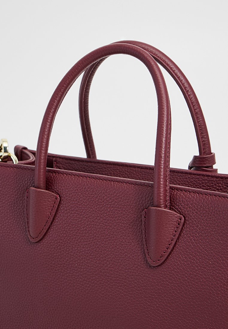 Burgunderfarbene Ledertasche mit strukturiertem Oberflächen, doppelten runden Griffen und geometrischen Akzenten. Verfügt über goldene Beschläge und eine strukturierte Form.