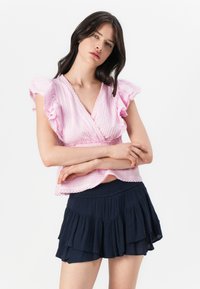 Blouse rose clair avec des manches à volants et un tissu texturé, associée à une jupe évasée en couches bleu marine foncé.