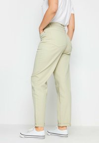 Jeans de tiro alto de color verde claro con un ajuste holgado, bajos ajustados y dos bolsillos traseros, combinados con zapatillas blancas.