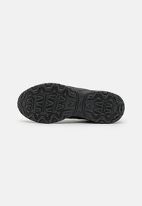 Sola de sapato atlético preto com padrão de pisada robusto, apresentando ranhuras em forma de V proeminentes e uma superfície texturizada para tração.
