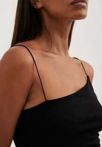 Černý top na ramínka s tenkými špagetovými ramínky, vyrobený z měkké látky. Vyznačuje se přiléhavým střihem a hladkou texturou.