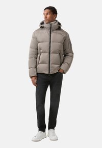 Pufferjakke i lys grå med lynlås front, justerbar hætte og sidelommer. Sammen med mørke jeans og hvide sneakers.