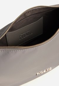 Bustina grigia in nylon con zip dorata e logo in rilievo all'interno. Interno foderato con tasca porta carte e superficie liscia.