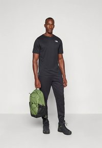 Svart t-shirt med korta ärmar, svarta byxor och en grön och svart ryggsäck. Outfiten har en enkel design och praktiska skor.