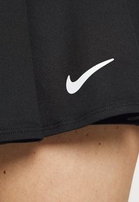 Svart idrottsimit med stretchigt tyg, med en vit Nike Swoosh-logga nära fållen. Slät yta och figurnära design.