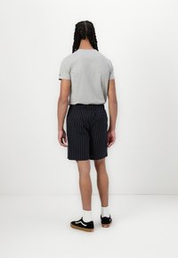 T-shirt gris à manches courtes, shorts noirs à rayures avec une taille élastique, associés à des baskets noires et des chaussettes blanches.