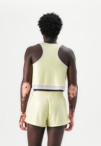 Lys gul netting trenings tank topp med en cropped design, kombinert med matchende shorts; har hvit kanting og elastisk midje.