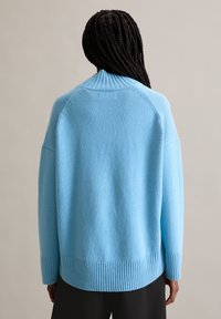 Lichtblauwe gebreide trui met een ribbelrand en manchetten, voorzien van een hoge kraag en verlaagde schouders. Soepele textuur en een losse pasvorm.