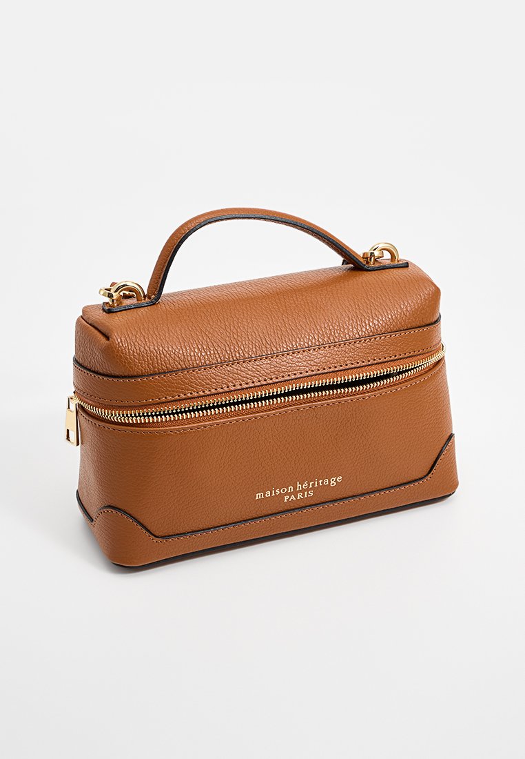 Sac en cuir marron au design structuré, avec fermeture éclair dorée et poignée supérieure. Présente un logo embossé à l'avant et une surface texturée.