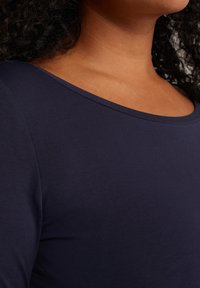 Camiseta de manga larga en azul marino, fabricada en una suave y elástica tela, con un amplio escote en forma de barco y un diseño ajustado que resalta su textura lisa.