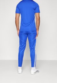 T-shirt de sport bleu et pantalon assorti, en tissu lisse. Le pantalon présente des rayures blanches sur les côtés et une coupe fuselée.