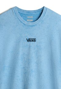 Vaaleansininen puuvillat-paita, jossa on tekstuuri, pyöreä kaula-aukko ja musta brodeerattu "VANS" -logo rinnassa. Koko-ämpäri "Pieni" näkyvissä.