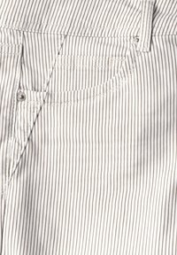 Tejido a rayas en blanco y marrón claro. Presenta un bolsillo frontal con un botón de metal y costuras visibles a lo largo de las uniones.