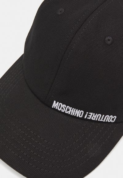 Casquette de baseball noire en tissu texturé avec une visière incurvée. Présente un texte brodé blanc indiquant "Moschino Couture !" sur le devant.