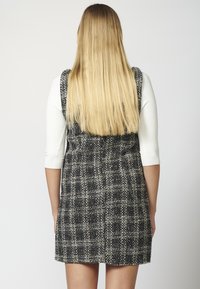 Vestito in tweed a scacchi bianco e nero con silhouette aderente, spalline larghe e superficie tessurizzata. Capelli lunghi e lisci biondi in vista.