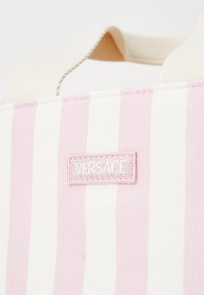 Canvas toteväska med växlande rosa och vita ränder, med en rektangulär rosa tygskylt präglad med "VERSACE."