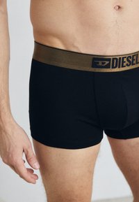 Black boxer briefs with a gold elastic waistband featuring the "Diesel" logo. Material appears smooth and fitted, with a classic design.