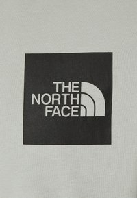 Lichtgrijze sweatshirt met een zwart vierkant logo waarop de tekst "THE NORTH FACE" staat en een halfcirkelvormig designelement. Katoenen materiaal.