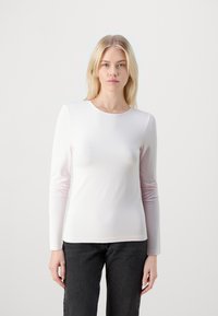 Lys rosa langermet topp med rund hals, laget av glatt stoff. Tettsittende design, kombinert med mørkegrå bukser.