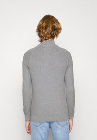 Grau gestrickter Pullover mit hohem Kragen, gerippter Textur und langen Ärmeln, entworfen mit einem lockeren Schnitt und gerader Saumlinie.