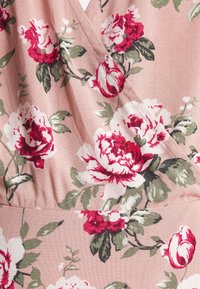Tissu rose avec un motif floral de grandes fleurs blanches et rouges et de feuilles vertes, montrant une couture et des fronces.