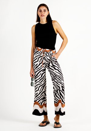 Black ribbed tank top paired with wide-leg zebra print pants featuring brown accents and a drawstring waist. Model holds sunglasses.