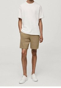 T-shirt en coton blanc, shorts beiges à la texture lisse et baskets blanches. Design simple, coupe décontractée, sans motifs ni accents visibles.