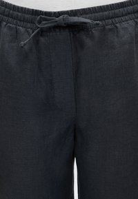 Pantalon en lin noir avec taille élastique et cordon noué, présenté de la taille jusqu'à mi-cuisse.