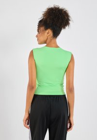 Green sleeveless top with a smooth texture, round neckline, and fitted silhouette. Paired with black track pants featuring vertical stripes.