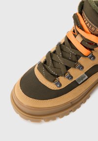 Scarpa da trekking marrone e verde con tessuto a rete, accenti in camoscio e lacci arancioni. Presenta occhielli in metallo e una suola in gomma spessa.