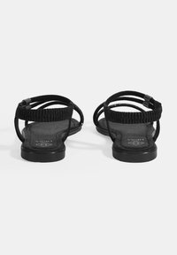 Schwarze Sandalen mit mehreren dünnen Riemen und flacher Sohle. Die Innensohle hat eine strukturierte Oberfläche und das Design ist minimalistisch.