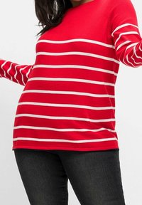 Rot gestreifter Strickpullover mit weißen horizontalen Streifen, rundem Halsausschnitt und langen Ärmeln. Kombiniert mit dunklen Jeans, vor einem schlichten Hintergrund präsentiert.