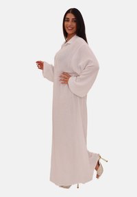 Robe longue et ample en tissu blanc doux et texturé. Comprend un col, des manches larges et un design fluide, associée à des chaussures à talons.
